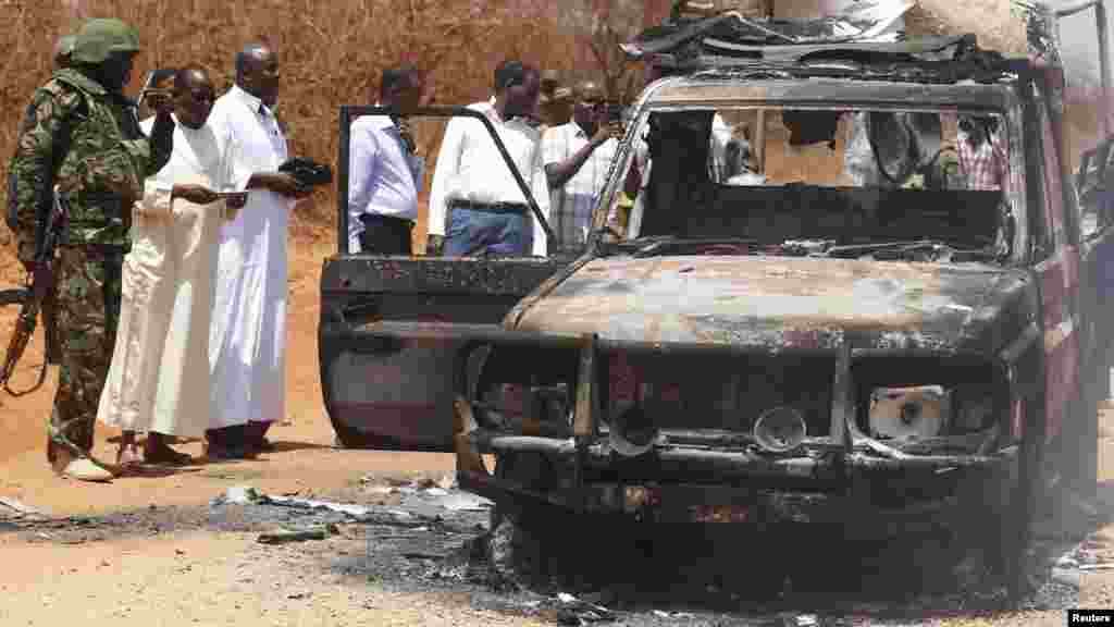 Des agents de sécurité et des membres du gouvernement inspectent une voiture de police qui a été brûlée lors d&#39;une attaque contre un convoi escortant le gouverneur de la région de Mandera Ali Roba près de la ville de Mandera, 13 Mars 2015.