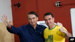 El favorito a la presidencia de Brasil, Jair Bolsonaro (izq.), del Partido Social Liberal y su hijo Flavio saludan a la prensa en un sitio de votación en Río de Janeiro, el 7 de octubre de 2018.