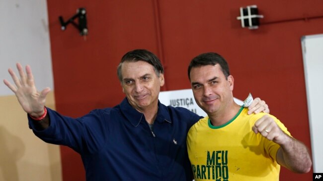El favorito a la presidencia de Brasil, Jair Bolsonaro (izq.), del Partido Social Liberal y su hijo Flavio saludan a la prensa en un sitio de votación en Río de Janeiro, el 7 de octubre de 2018.