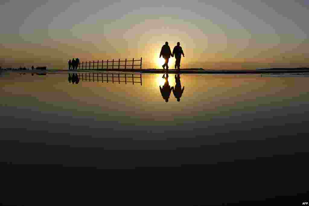 Palestinians walk through a wet street after the rain as the sun sets over the Al-Shatee refugee camp in Gaza City.