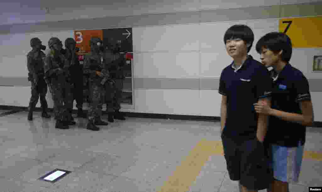 Students walk past South Korean soldiers wearing gas masks during an anti-terror drill at a subway station in Seoul during joint South Korean-U.S. military drills, August 19, 2013.