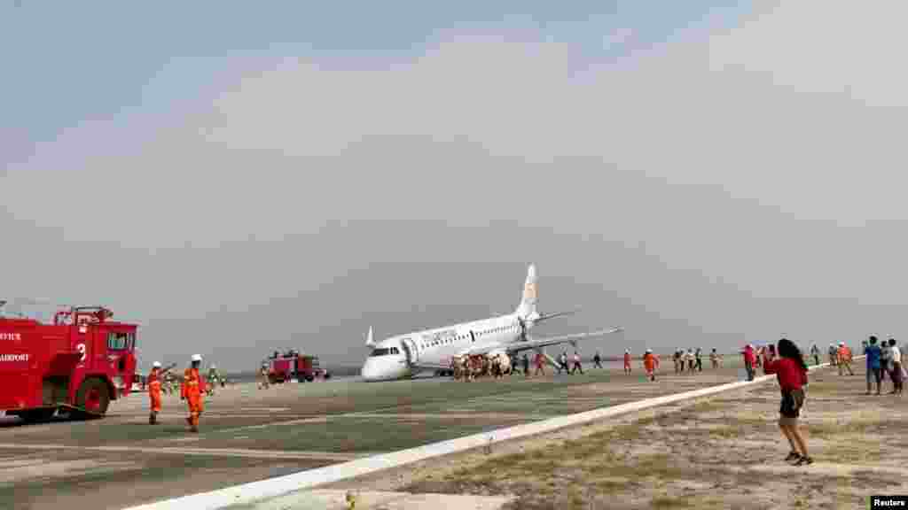 An evacuated passenger records on her phone as firefighters arrive at the scene after Myanmar National Airlines flight UB103 landed without a front wheel at Mandalay International Airport, Myanmar, in this still image taken from social media.