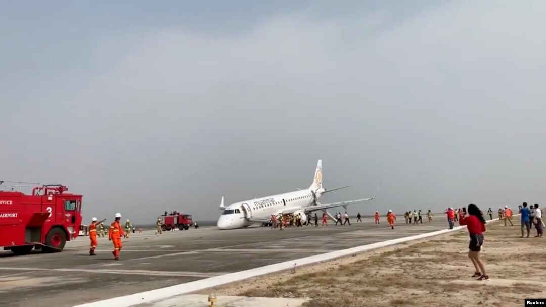 An evacuated passenger records on her phone as firefighters attend to the scene after Myanmar National Airlines flight UB103 landed without a front wheel at Mandalay International Airport in Tada-U, Myanmar, May 12, 2019 in this still image taken from soc