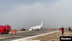 An evacuated passenger records on her phone as firefighters attend to the scene after Myanmar National Airlines flight UB103 landed without a front wheel at Mandalay International Airport in Tada-U, Myanmar, May 12, 2019 in this still image taken from social media video.