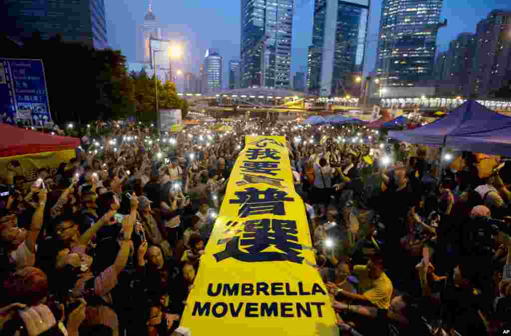 Para demonstran pro-demokrasi mengembangkan spanduk kuning bertuliskan &quot;Saya ingin hak pilih universal&quot; dalam demonstrasi di daerah-daerah yang diduduki di luar kantor-kantor pusat pemerintahan di distrik Admiralty, Hong Kong (28/10).&nbsp;(AP/Kin Cheung) 