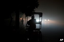 FILE - A rickshaw puller waits for customers along a roadside amidst heavy smog in New Delhi, India, Nov. 6, 2016.