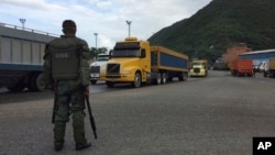 FILE – A National Guard soldier watches over cargo trucks leaving the port Dec. 19, 2016, in Puerto Cabello in Venezuela, the port city that handles the majority of the country's food imports. Across the chain of command, from high-level generals to the lowest foot soldiers, military officials reportedly are using their growing power over the food supply to siphon off wealth for themselves.