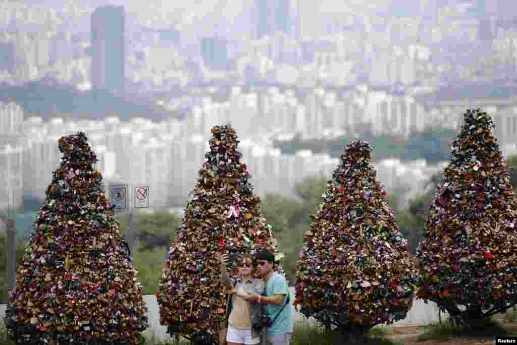 &#39;사랑의 자물쇠&#39; 나무들이 줄 서 있는 서울 남산 꼭대기 엔서울타워에서 한 연인이 셀카를 찍고 있다. 이곳은 연인들이 사랑의 징표로 나무에 자물쇠를 장식하면서 관광명소가 되었다.