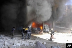 In this photo released on Feb. 20, 2018 provided by the Syrian Civil Defense group known as the White Helmets, shows members of the Syrian Civil Defense extinguishing a store during airstrikes and shelling by Syrian government forces, in Ghouta, a suburb of Damascus, Syria