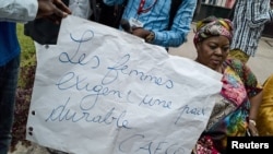 FILE - A Congolese woman holds a placard saying "Women require stable peace" as she and others sit in protest during talks between the opposition and the government of President Joseph Kabila outside the Conference episcopale nationale du Congo (CENCO) headquarters in the Democratic Republic of Congo's capital, Kinshasa, Dec. 31, 2016.