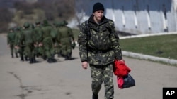 Seorang tentara Ukraina berjalan melewati tentara Rusia yang tengah berbaris menuju barak mereka di luar markas militer di Perevalne, Krimea, 21 Maret 2014. 