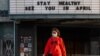 En esta foto del 21 de marzo de 2020, una mujer camina usando una máscara protectora contra el coronavirus frente a un teatro cerrado en Koreantown, Los Ángeles.