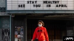 En esta foto del 21 de marzo de 2020, una mujer camina usando una máscara protectora contra el coronavirus frente a un teatro cerrado en Koreantown, Los Ángeles.