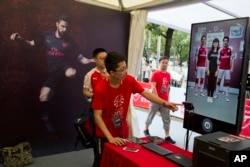FILE - A worker directs a fan of Arsenal into position for an augmented reality photo session during an exhibition ahead of an Arsenal vs. Chelsea soccer match in Beijing, China, July 21, 2017.