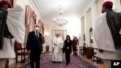 In this photo provided by the Greek President's office, Greece's President Katerina Sakellaropoulou and Pope Francis arrive to a ceremony at the Presidential Palace in Athens, Greece, Dec. 4, 2021.