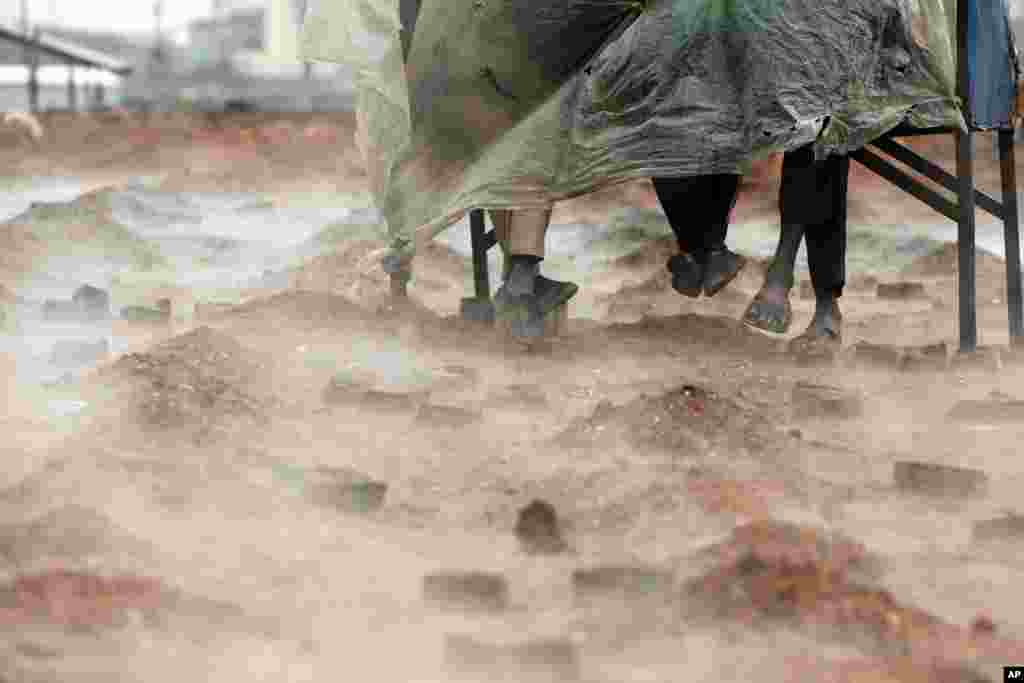 Hindistopnlik migrant ishchilar g&#39;isht pechi yonida yomg&#39;irdan pana qilib plyonka ostida o&#39;tiribdi. Katmandu, Nepal