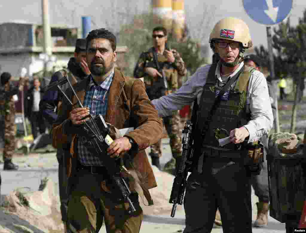 Seorang petugas keamanan Inggris, kanan, mengawal seseorang yang selamat dari rongsokan kendaraan milik Kedutaan Besar Inggris yang diserang bom bunuh diri di Kabul, 27 November 2014.