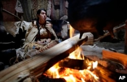 In this Nov. 15, 2018, photo, Mashpee Wampanoag Kerri Helme, of Fairhaven, Mass., uses plant fiber to weave a basket while sitting next to a fire at the Wampanoag Homesite at Plimoth Plantation, in Plymouth, Mass.