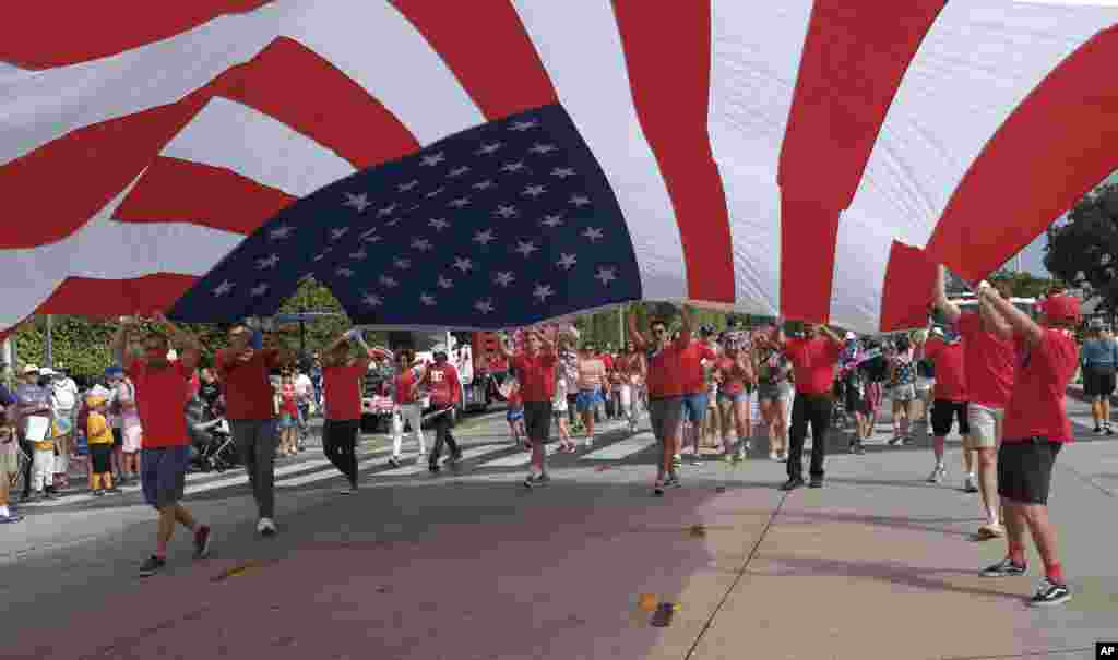 美国加州圣莫妮卡的国庆游行，人们举着巨大的美国国旗（2017年7月4日）。