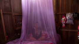 FILE - In this Tuesday, Sept. 29, 2020 file photo, Valentina Esperanza, who is recovering from dengue, sits on her bed protected by mosquito netting as she watches a television program at her home in Pucallpa, in Peru's Ucayali region.