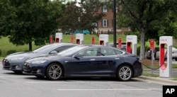 FILE - Telsa cars recharge at a Tesla station at a shopping center in Charlotte, N.C., June 24, 2017.