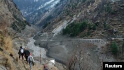 Orang-orang berjalan melewati bendungan yang hancur setelah gletser Himalaya pecah dan menabrak bendungan di Desa Raini Chak Lata di distrik Chamoli, negara bagian utara Uttarakhand, India, 7 Februari 2021. (Foto: Reuters)