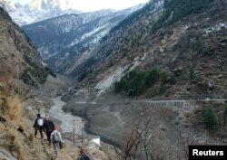 Orang-orang berjalan melewati bendungan yang hancur setelah gletser Himalaya pecah dan menabrak bendungan di Desa Raini Chak Lata di distrik Chamoli, negara bagian utara Uttarakhand, India, 7 Februari 2021. (Foto: Reuters)