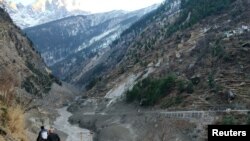 Watu wakipita eneo la bwawa lililoharibiwa na kuanguka kwa theluji huko kijiji cha Raini Chak Lata , wilaya ya Chamoli, kaskazini mwa jimbo la Uttarakhand India, 7 Februari 2021. (Foto: Reuters)