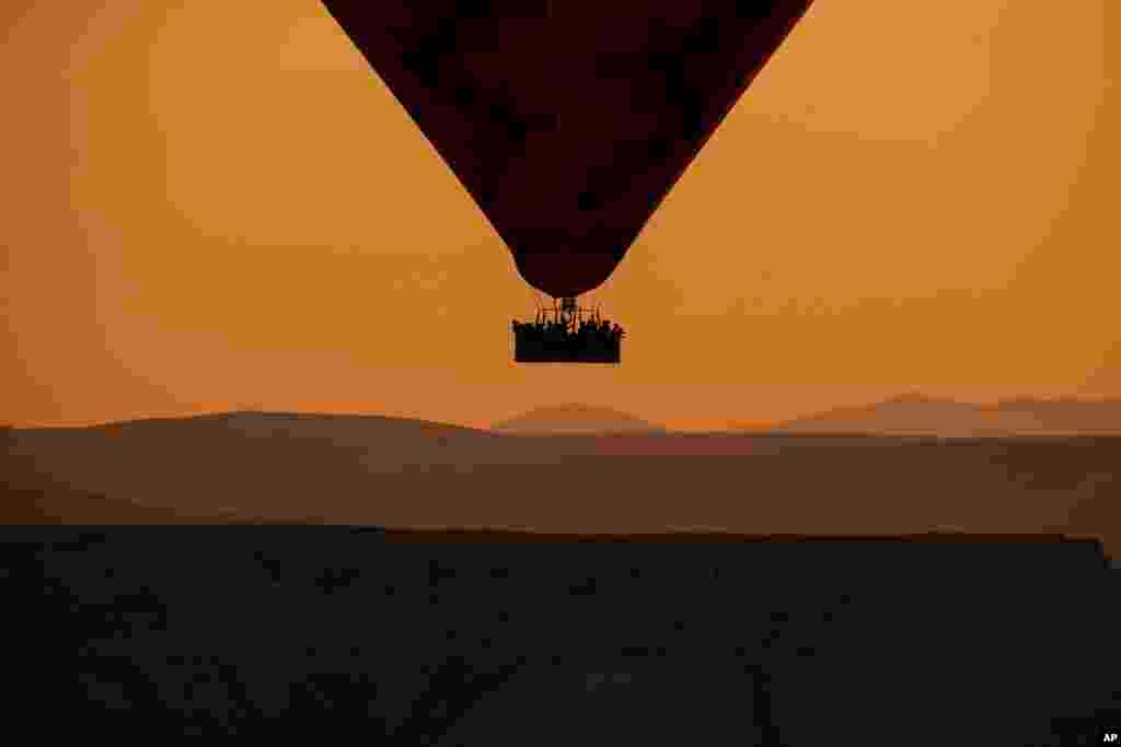 A hot air balloon, carrying tourists, rises into the sky at sunrise in Cappadocia, central Turkey.