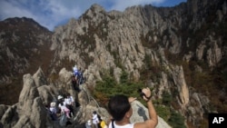 FILE – A North Korean man records video while climbing his country’s Mount Kumgang in 2012. Some South Korean firms hope to resume a project involving tours to that area. 