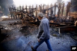 Homeowner Alan Barnard walks past the remains of his RV from a wildfire in the Lake View Terrace area of Los Angeles, Dec. 5, 2017.