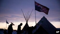 FILE - In this Dec. 2, 2016, file photo, travelers arrive at the Oceti Sakowin camp where people have gathered to protest the Dakota Access oil pipeline as they walk into a tent next to an upside-down american flag in Cannon Ball, N.D.