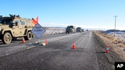A convoy of armored vehicles and SUVs rolls past a barricade on the road near the Malheur National Wildlife Refuge near Burns, Ore., Jan. 30, 2016.