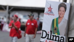 People walk next to an official photography of Brazil's suspended President Dilma Rousseff, with a text written in Portuguese that reads "Dilma our president," at a camp in Brasilia, Brazil, Sunday, Aug. 28, 2016.