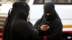 FILE - A burqa-clad Indian woman checks her phone at a street in Hyderabad, India, March 24, 2015. 