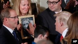 Jeanne Moser, center, of East Kingston, New Hampshire, watches as President Donald Trump reaches out to touch a photo of her son, Adam Moser, during an event to declare the opioid crisis a national public health emergency, in the East Room of the White House in Washington, Oct. 26, 2017.