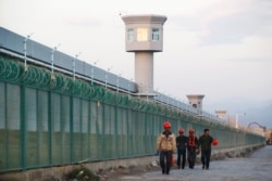 Para pekerja berjalan menyusuri tembok pembatas pusat pendidikan kejuruan di Dabancheng, Wilayah Otonomi Uighur, China, 4 September 2018. (Foto: Reuters)