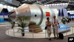 FILE - Visitors sit besides a model of Chinese made Tiangong 1 space station at the 8th China International Aviation and Aerospace Exhibition, known as Airshow China 2010, in Zhuhai city, south China, Guangdong province, Nov. 16, 2010.