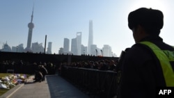 FILE - A security guard watches as mourners place flowers and burn incense at the site of a New Year's Eve stampede at the Bund in Shanghai, China, Jan. 2, 2015. 