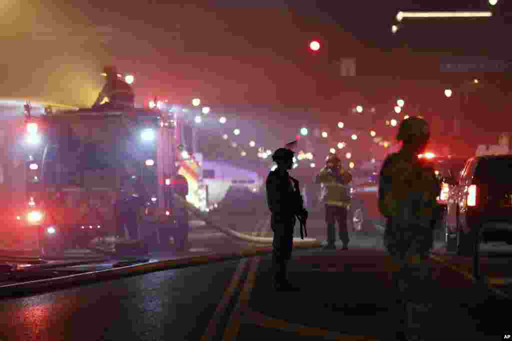 မီးလောင်နေသည့် ဓာတ်ဆီဆိုင်တခုကို မီးငြိမ်းသတ်နေသည့် မီးသတ်ကားများအနီး အစောင့်ချထားသည့် လုံခြုံရေးတပ်ဖွဲ့များ။ (Minneapolis) (မေ ၂၉၊ ၂၀၂၀) 