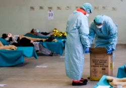 Paramedics carry an hazardous medical waste box as patients lie on camping beds, in one of the emergency structures that were set up to ease procedures at the Brescia hospital, northern Italy, Thursday, March 12, 2020. (AP Photo/Luca Bruno)