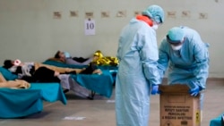 Paramedics carry an hazardous medical waste box as patients lie on camping beds, in one of the emergency structures that were set up to ease procedures at the Brescia hospital, northern Italy, Thursday, March 12, 2020. (AP Photo/Luca Bruno)