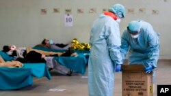 Paramedis membawa kotak limbah medis berbahaya sementara pasien virus corona berbaring di tempat tidur di Rumah Sakit Brescia, Italia, Kamis, 12 Maret 2020. (Foto: AP/Luca Bruno)