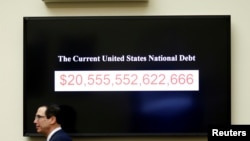 2018年2月6日美国财政部长努钦在美国华盛顿国会山作证时走过显示美国国债的屏幕。