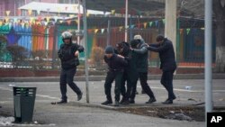 A police officer escorts a group of detained protesters in Almaty, Kazakhstan, Jan. 6, 2022. 