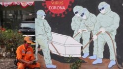 A street sweeper checks his mobile phone as he takes a break near a coronavirus-themed mural in Jakarta, Indonesia.
