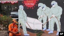 A street sweeper checks his mobile phone as he takes a break near a coronavirus-themed mural in Jakarta, Indonesia.