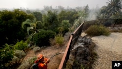 A firefighter from the California Conservation Crops Alder Camp works to put out wildfire hot spots, Dec. 16, 2017, in Montecito, Calif.