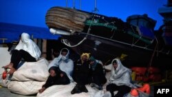 Les migrants sont assis à bord du MV Aquarius, un navire de sauvetage affrété par SOS-Méditerranée et Médecins Sans Frontières (MSF), en Méditerranée, à destination de l'Italie le 9 mai 2018. La Garde côtière italienne a accordé l'autorisation à 105 migra
