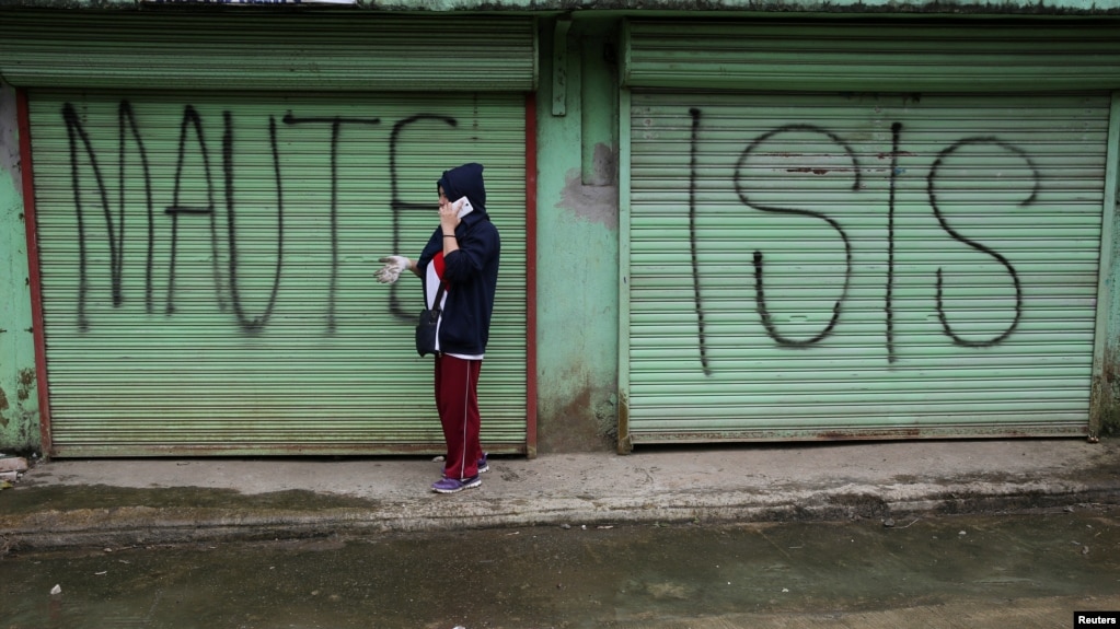 FILE - A person is seen using a mobile phone while passing a shuttered store front with "MAUTE-ISIS" graffiti, in Marawi city, southern Philippines, Oct. 20, 2017.